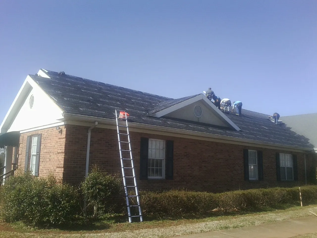 Crew tearing shingles off a brick ranch roof with a ladder set — Emergency Roof Repair work by our crew in Olean