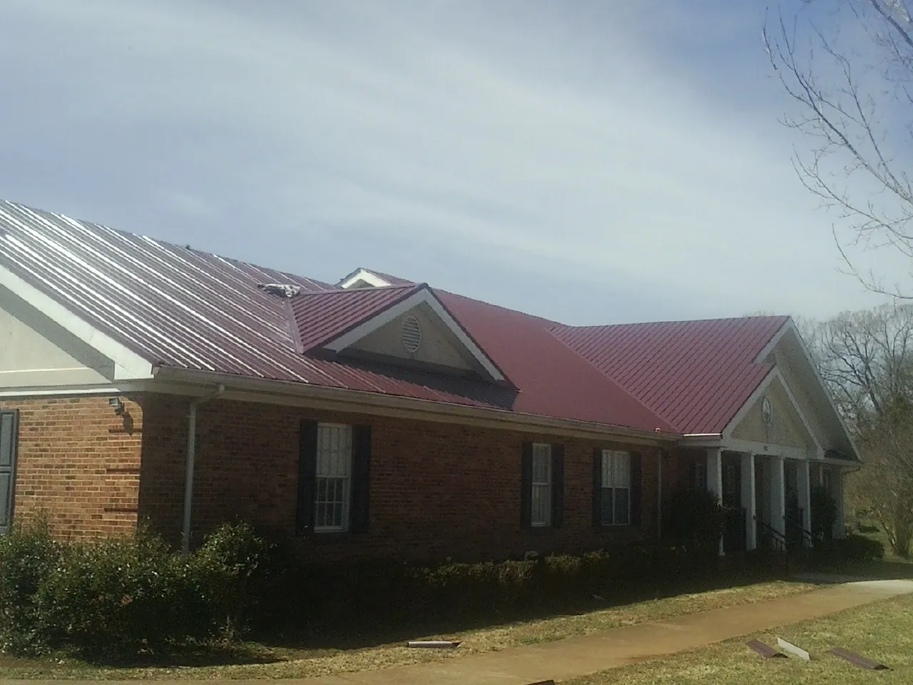 Red metal roof with gabled entries on a long brick building, from a Hail Damage Roof Repair job in Olean