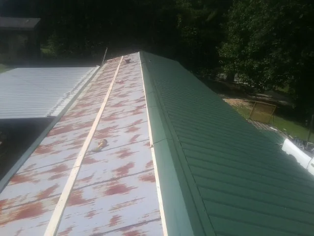 Old rusted panels beside newly installed green metal roofing — Wind Damage Roof Repair by Roofing Brothers in Olean