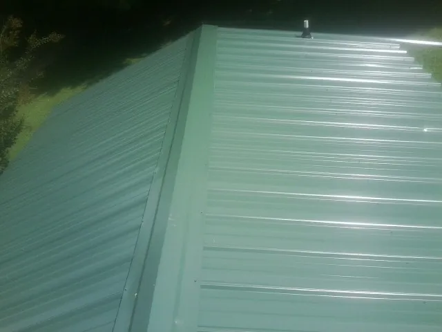 New green metal panels meeting at the ridge of a roof — Flat Roof Repair work by our crew in Olean